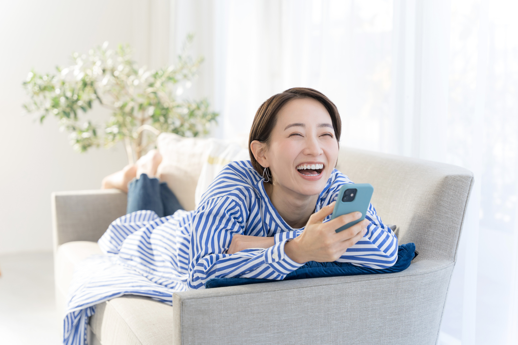 ソファーでスマートフォンをみている笑顔の女性