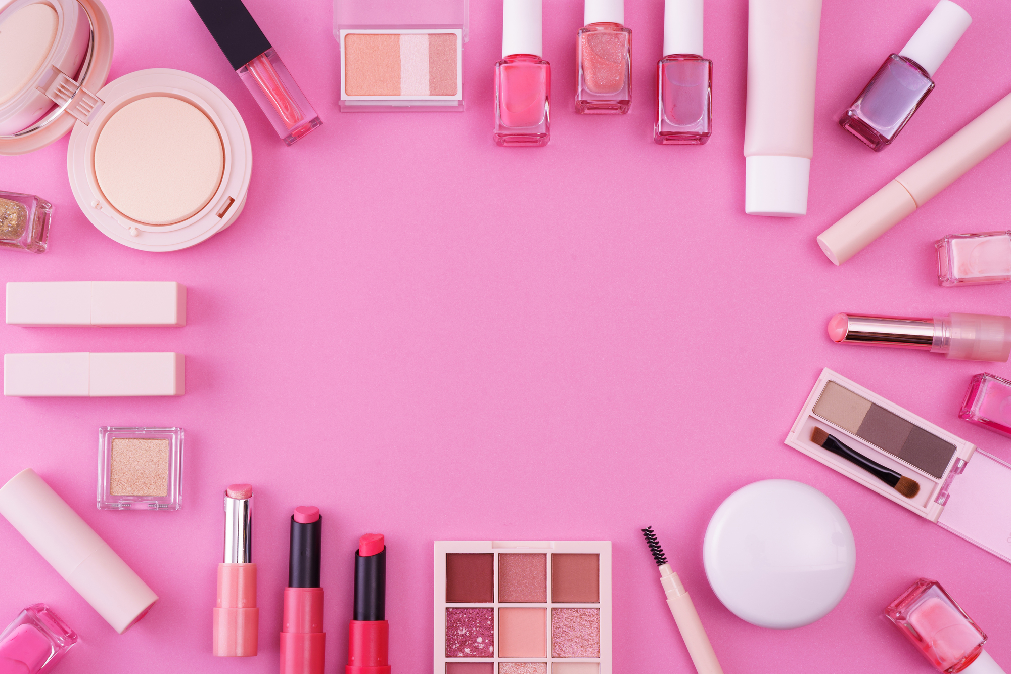 ピンク色の壁を背景に中央部分を除いて縁どるように並べられた化粧品の数々